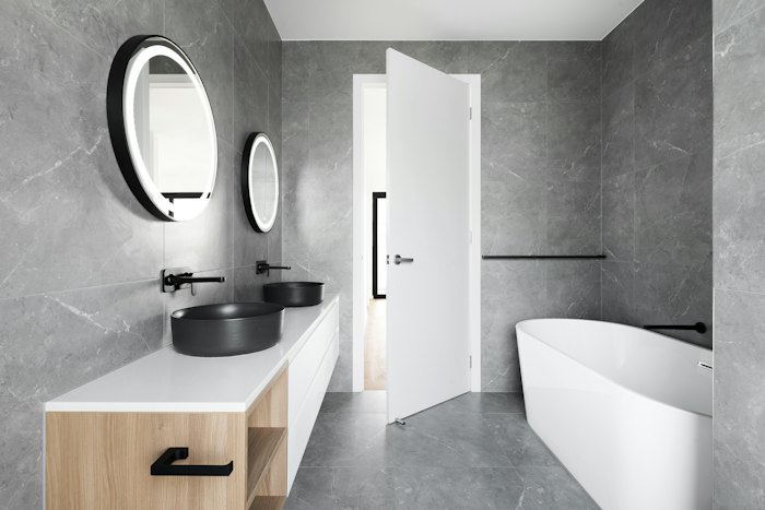 Grey stone-tiled bathroom with a double vanity and freestanding tub.
